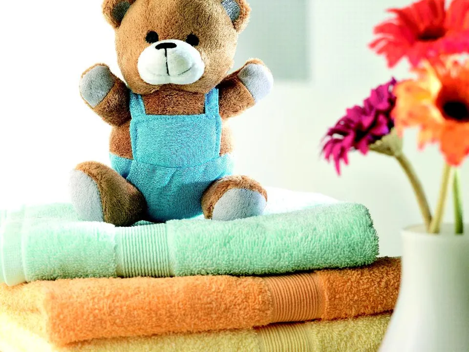 Ours en peluche avec salopette bleu clair, posé sur des serviettes