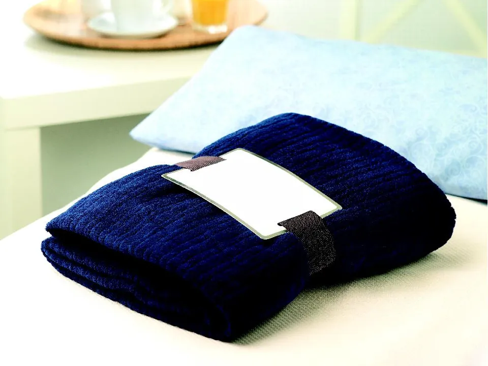 Plaid bleu marine plié sur un lit, avec sa bande pour le marquage