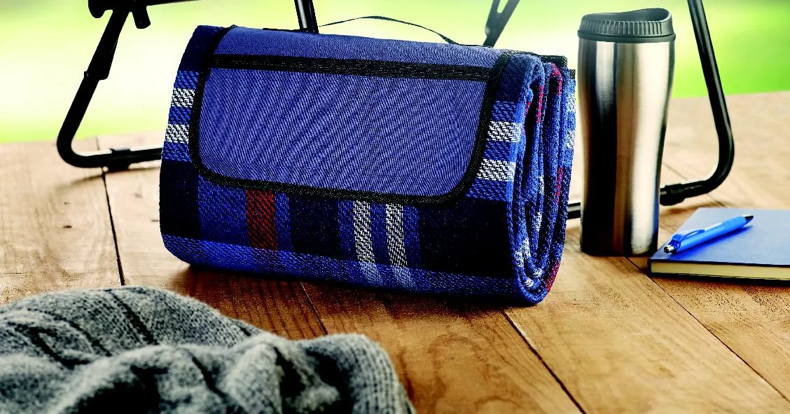 Plaid à carreaux roulé sur une table en bois, à côté d'une bouteille isotherme et d'un carnet